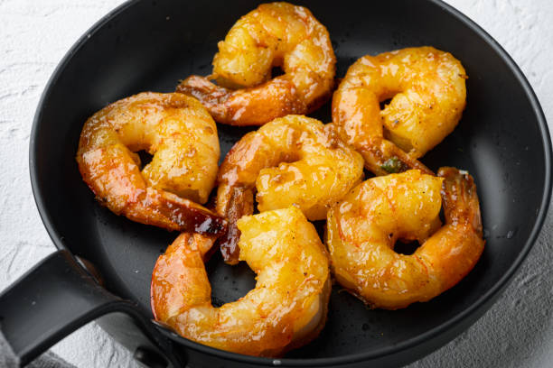 istock Freshly cooked tiger shrimps with Mango chutney  and curry, on frying iron pan, on white background 1414954244