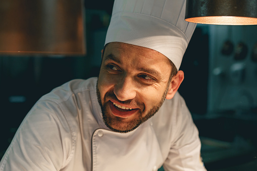 Close up of smiling male chef in uniform standing on kitchen of restaurant. High quality photo
