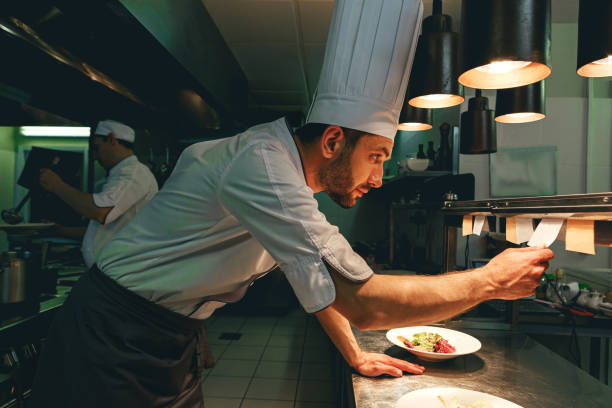 Handsome Chef cook in uniform checking the order at the restaurant kitchen Handsome Chef cook in uniform checking the order at the restaurant kitchen. High quality photo restaurant labor union stock pictures, royalty-free photos & images