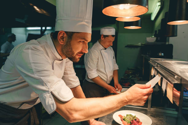Handsome Chef cook in uniform checking the order at the restaurant kitchen Handsome Chef cook in uniform checking the order at the restaurant kitchen. High quality photo restaurant labor union stock pictures, royalty-free photos & images