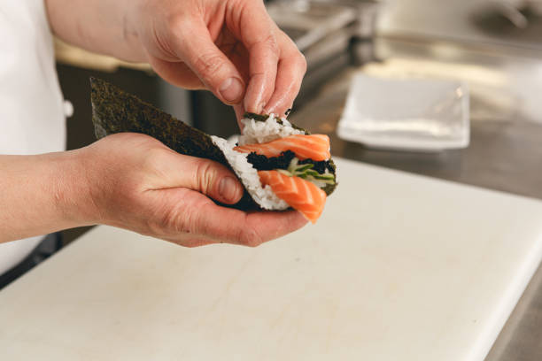 Chef hands cooking sushi with rice, salmon and nori on kitchen of japanese restaurant stock photo