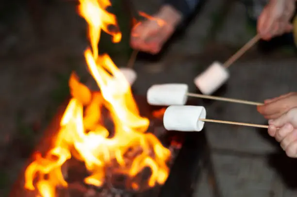 Photo of children's hands hold large pieces of marshmallow on wooden skewers over the fire - a sweet delicacy popular in the USA for barbecue. selective focus.