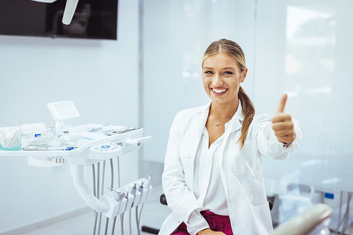 Portrait of female dentist .She standing in her dentist office. Young female dentist in white coat at workplace. Space for text. People, medicine, stomatology and healthcare concept