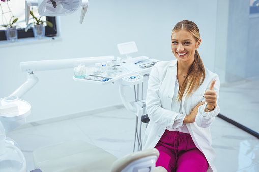 People, medicine, stomatology and healthcare concept - happy young female dentist with tools over medical office background. Portrait of female dentist smiling with arms crossed in dental clinic