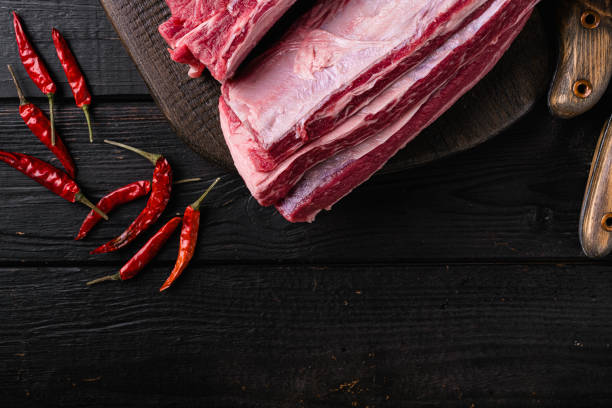 Raw beef short ribs, on black wooden table background, top view flat lay, with copy space for text.