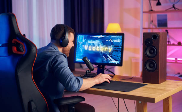 istock View from behind. Online streamer playing FPS shooter game at home 1414962263