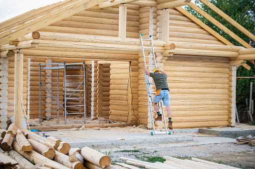 Cinstruction worker on ladder building a log cabin.