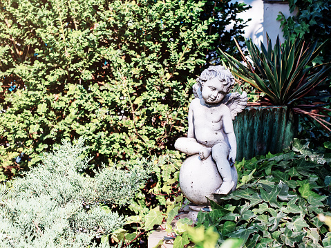 White stained figurine of a baby angel sitting on a ball in a green garden