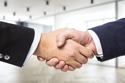 Two content businessmen sitting and shaking hands over a conference table, copy space.