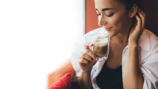 istock Young woman drinking coffee cappuccino sitting near window. 1414967136