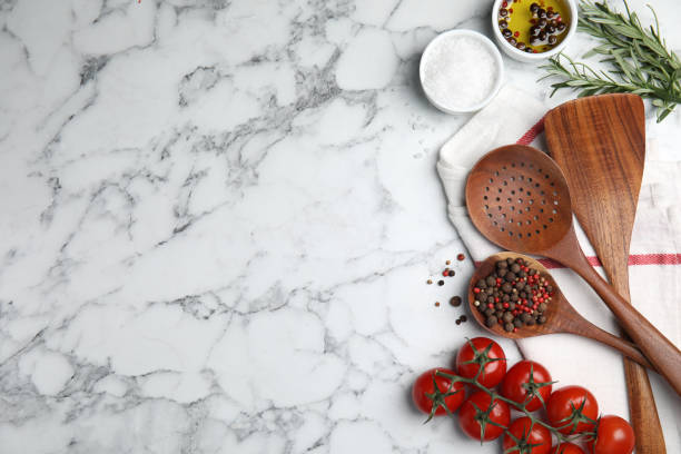Flat lay composition with cooking utensils and fresh ingredients on white marble table. Space for text
