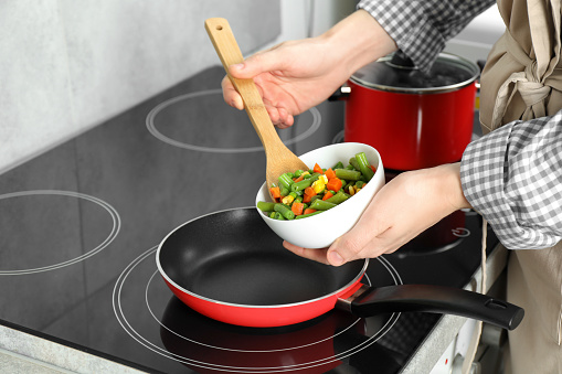 Woman putting tasty vegetable mix in frying pan at home, closeup