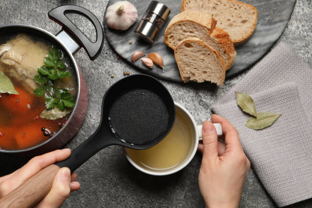 istock Woman pouring hot delicious bouillon into cup at grey table, top view 1414970308