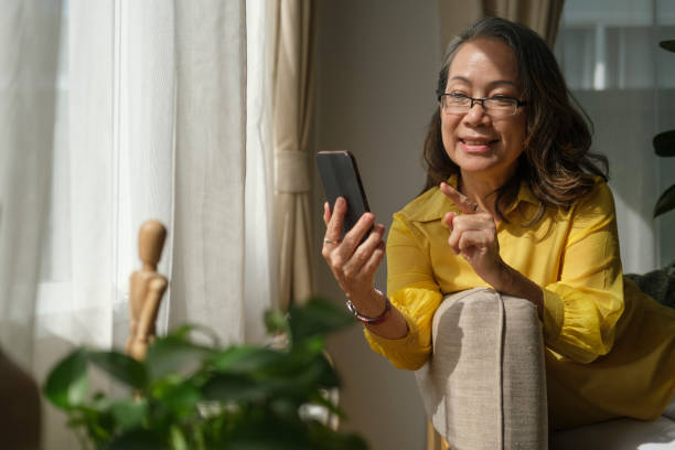 istock Happy middle aged woman resting on comfortable couch in bright living room and using smart phone. 1414970339