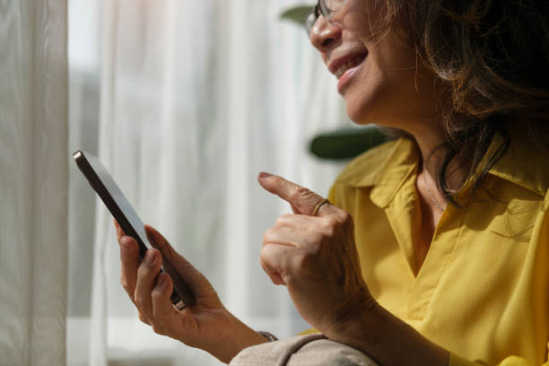 istock Happy middle aged woman resting on comfortable couch in bright living room and using smart phone. 1414970900