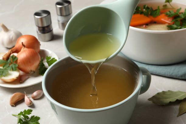 istock Pouring hot delicious bouillon into cup on light grey table, closeup 1414971058