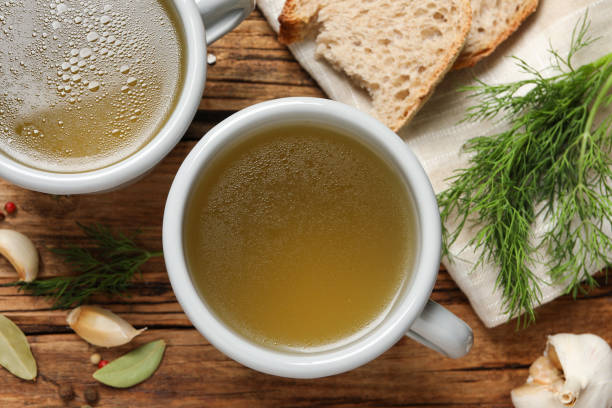 istock Hot delicious bouillon in cups on wooden table, flat lay 1414971096
