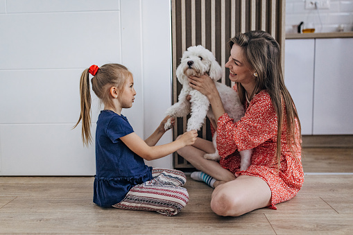 Mother and daughter sitting on the floor at home and playing with little dog