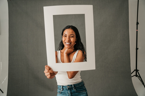 Happy smiling African American female framing her face with a white frame in the studio . High quality photo
