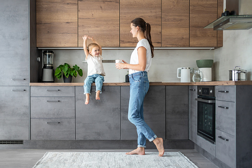 Little girl and happy mother with a cup of milk have a fun at home kitchen . High quality photo