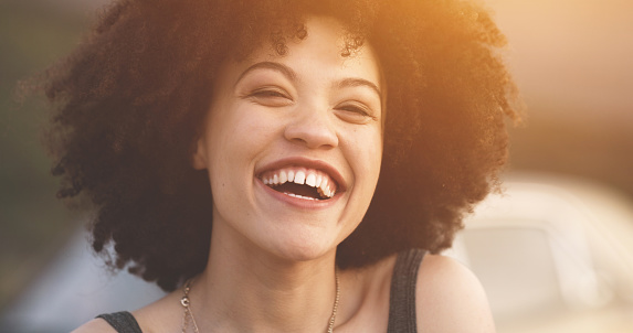 Cheerful, carefree and laughing afro woman smiling and feeling happy while standing outdoors with lens flare. Portrait of young female having fun and enjoying travel, adventure and free time on trip