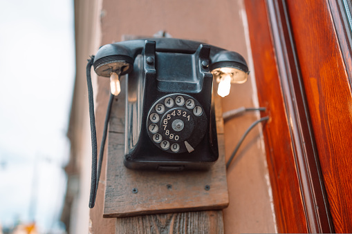 Old broken retro style dial black phone on bricks wall at street