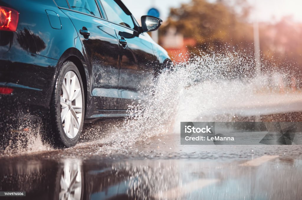 Car driving through the puddle and splashing by water. Car driving through the puddle and splashing by water. Dangerous situation. Concept of road safety. Rain Stock Photo