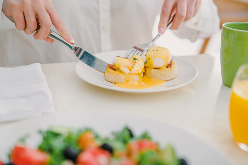 Closeup of a woman  cutting Eggs Benedict served with bacon and Hollandaise sauce