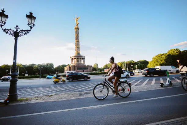 Commuter or a tourist woman on the bicycle in Berlin district of Kreuzberg, on a bright and sunny summertime day, riding through the traffic.