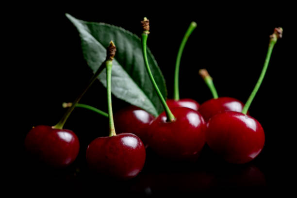 istock Red cherry berries with leaves on a black background with mirror. Three cherries 1414981936
