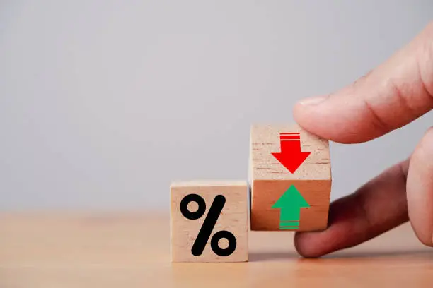 Photo of Hand flipping wooden cube block to change between up and down with percentage sign symbol for increase and decrease financial interest rate and business investment growth from dividend concept.