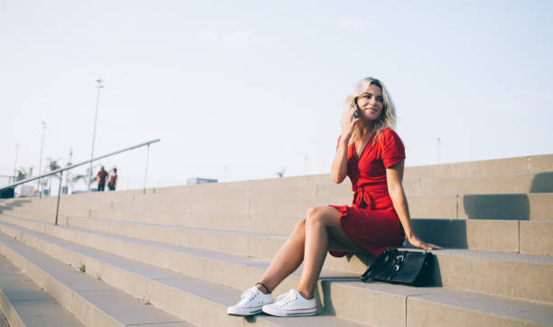 istock Young Caucasian traveller enjoying conversation calling during resting break at urban stairs, charming woman using mobility application and 4g in roaming for making international communication 1414984337