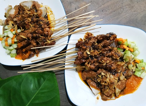 Indonesian food: beef satay on plate, served with peanut sauce and pickles.