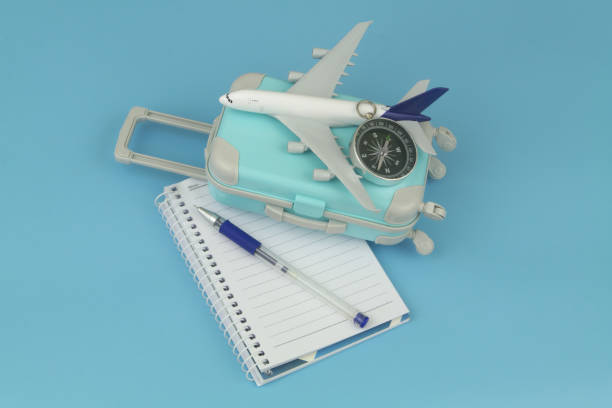 Airplane with compass on suitcase and notebook with pen.