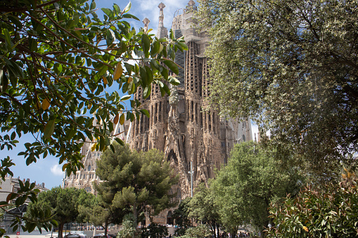 10th June, 2022 - Detail of a sculpture on the world famous La Sagrada Familia Cathedral in Barcelona in Spain shot through trees