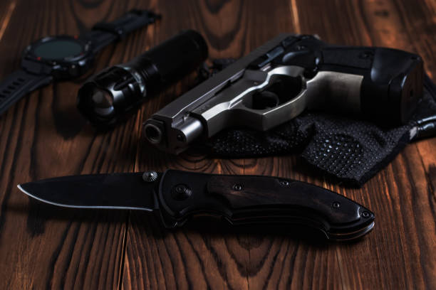 istock Folding pocket knife with pistol and flashlight on wooden background 1414988591