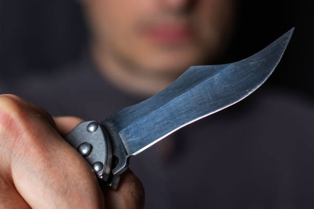 istock Closeup male hand holds sharp knife against black background 1414988630