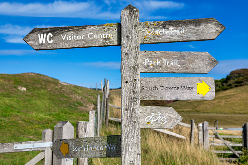 A weathered, wooden signpost points the way of Hadrian's Wall Path, a National Trail in the UK. Taken on a sunny day with a blue sky.