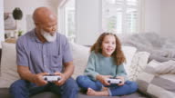 istock Grandfather playing video games with his granddaughter bonding and having fun at home together. Carefree and happy African American old man enjoying some entertainment with a young girl 1414988769