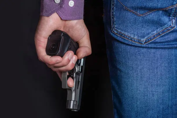 A man holding a gun in his hand behind his back, close-up view. Concepts: crime, attempted murder, a gunshot wound, the killer, robbery