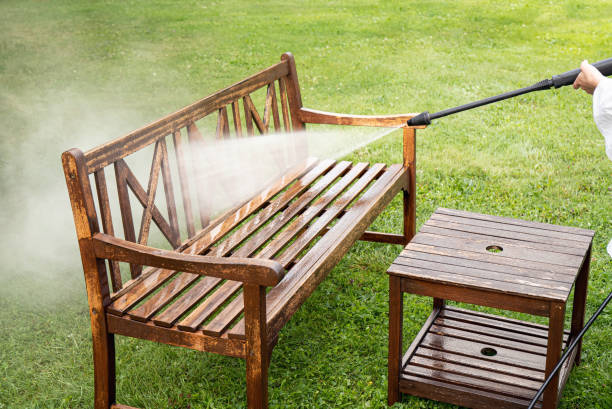 Close up view of person working cleaning pressure washing wooden garden furniture bench outdoors in summer. stock photo