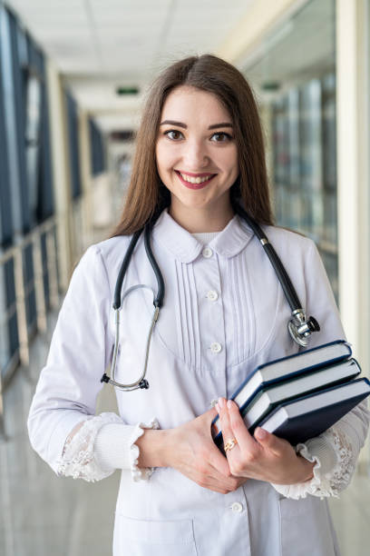 female doctor holding  book or magazine and walking down the med corridor to examine patients - medical student healthcare and medicine book education imagens e fotografias de stock