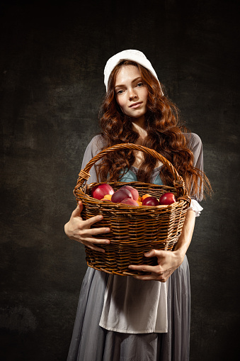 Girls with plums. Young charming redhair girl with long curly hair like girl of renaissance eras isolated on dark background. Comparison of eras, beauty, history, art, creativity.
