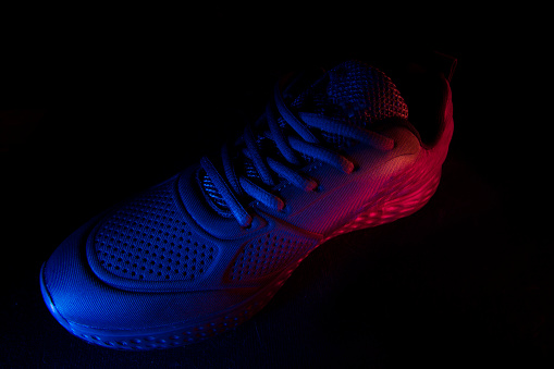 On a black background, sneakers illuminated by blue and red light filters. Beautiful sports shoes.