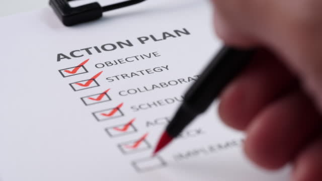 Close-up businessman tick off or marking with red pen on action plan checklist, checkbox after completing task on white paper. Selective focus 4K resolution. Concept of Action Plan, Checklist