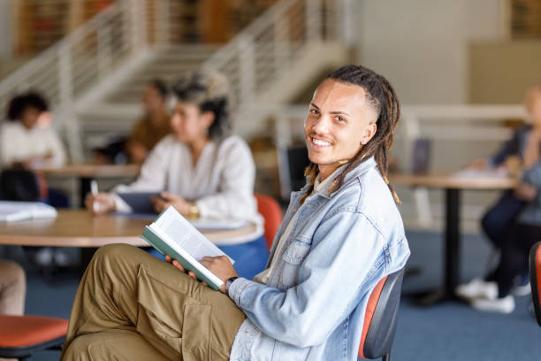 istock Smiling young man with dread locs reading a book at the livrary 1414998486