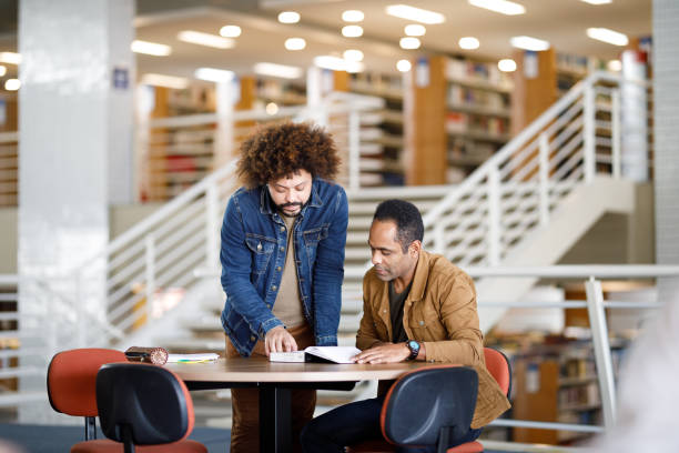 istock Curly haired man helping another student at the library 1414998492