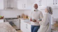 istock Senior interracial couple laughing, bonding and talking while drinking coffee together in the morning. Happy, smiling and cheerful retired husband and wife enjoying a beverage and making conversation 1414999998