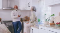 istock Happy, laughing and talking interracial couple bonding, feeling in love and enjoying cups of coffee in home kitchen. Mature or retired man and woman joking together and sharing funny stories 1415000191