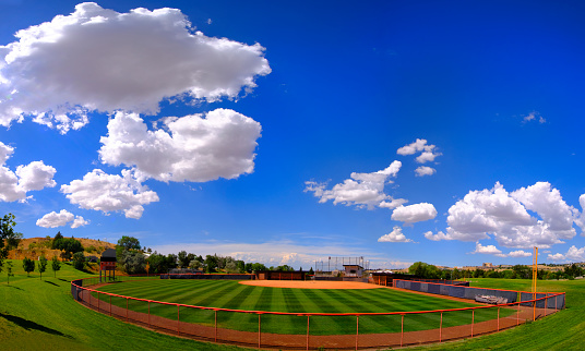 Manicured mowed grass lines on a baseball field diamond with blue sky and clouds summer day